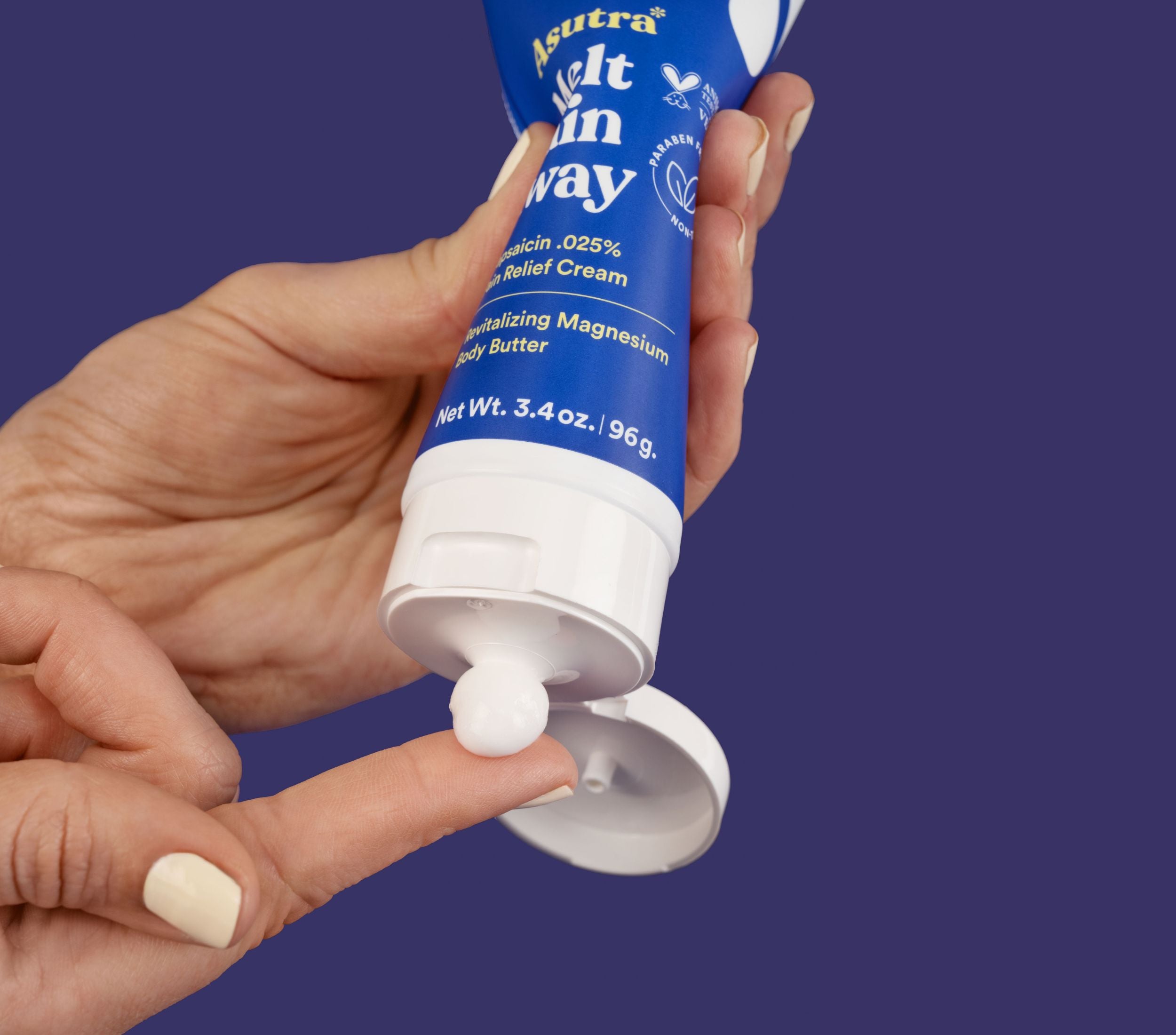 Hand holding a tube of Asutra Melt Pain Away Body Butter, dispensing a small amount of cream for muscle relief.