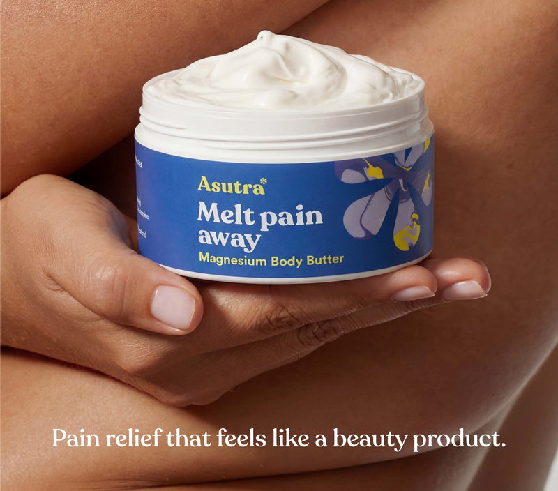 A person holds a jar of Asutra Melt Pain Away Magnesium Body Butter, promoting pain relief with a soothing texture.
