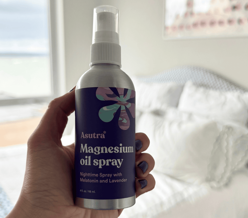 Hand holding a 4 fl oz (118 ml) bottle of Asutra Magnesium Oil Spray with melatonin and lavender, designed for nighttime relaxation.