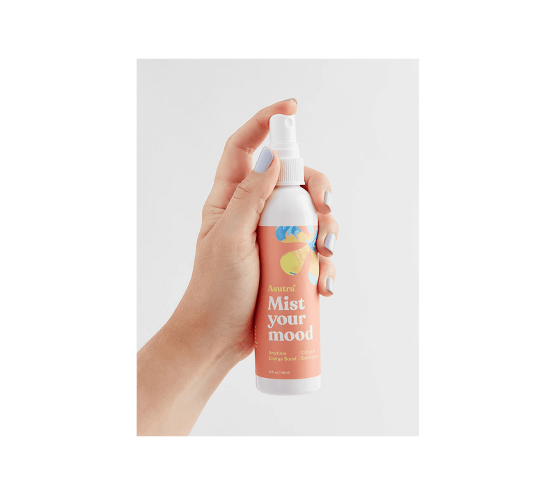 Hand holding a white spray bottle labeled "Mist your mood" with citrus and eucalyptus illustrations, promoting energy boost aromatherapy.