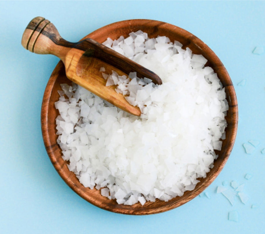 Wooden bowl filled with white magnesium flakes, placed on a light blue background.
