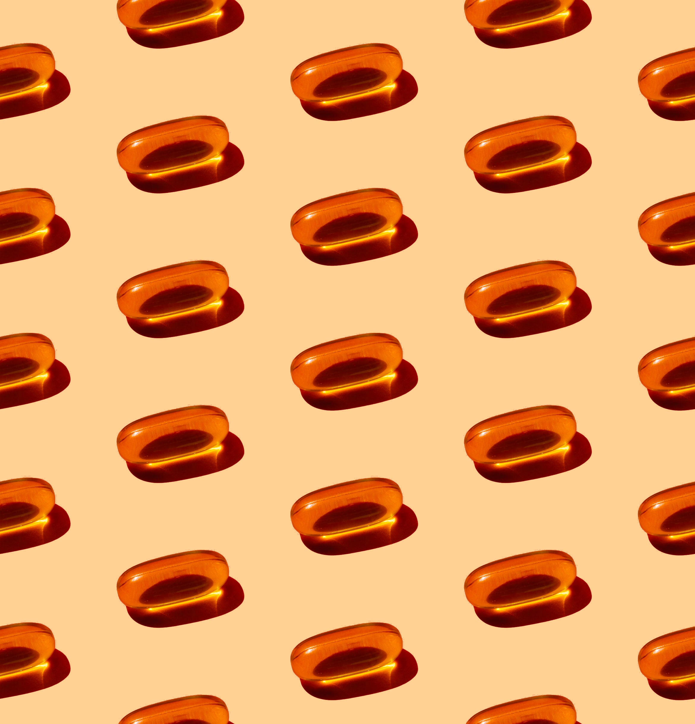 Rows of orange vitamin E capsules arranged on a light peach background.