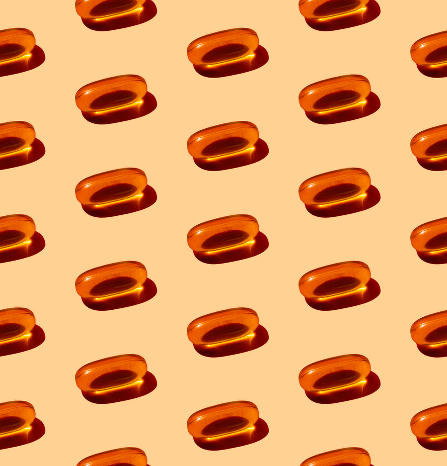 Rows of orange vitamin E capsules arranged on a light peach background.