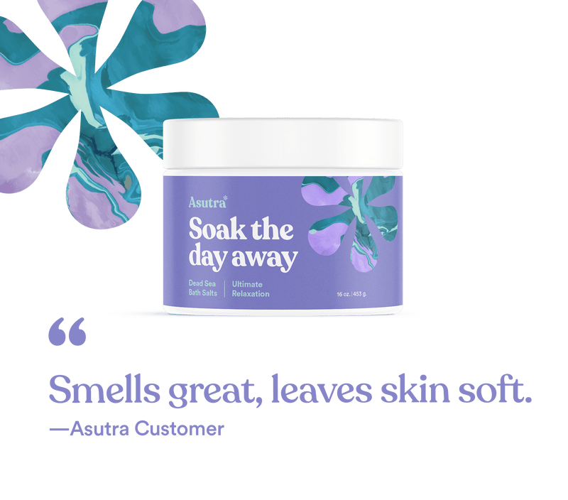 A jar of Asutra Lavender Ultimate Relaxation Bath Salts with a purple label, lavender flower illustration, and a customer quote: "Smells great, leaves skin soft.