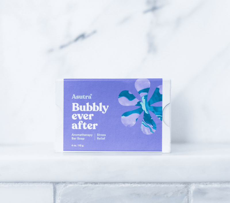 A lavender-colored box of Asutra Bubbly Ever After aromatherapy stress relief bar soap against a white marble background.