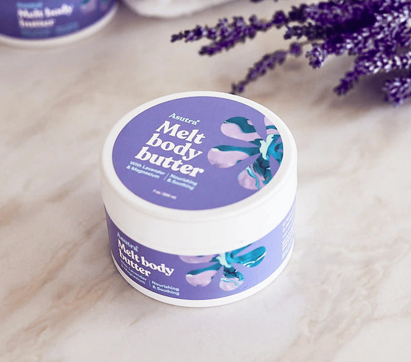 Lavender body butter with magnesium in a purple container, featuring floral design, on a marble surface with lavender flowers nearby.
