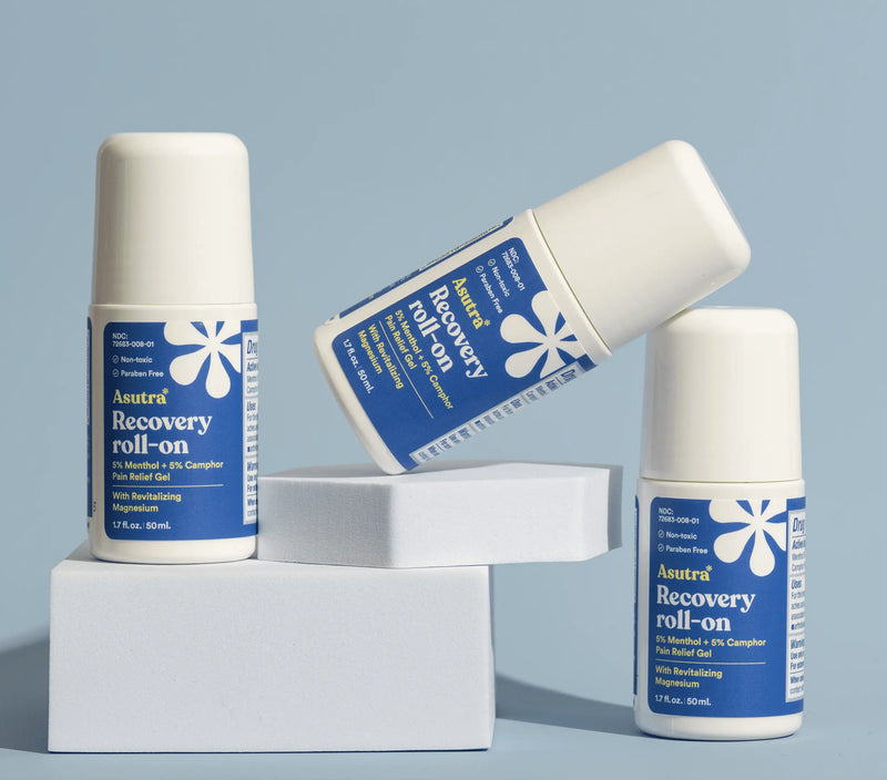 Three white roll-on bottles of Asutra Recovery Pain Relief Gel with blue labels, arranged on white blocks against a light blue background.