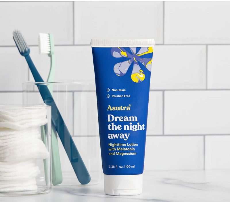 Blue tube of Asutra Dream the Night Away lotion with melatonin and magnesium, labeled as non-toxic and paraben-free, on a bathroom counter.