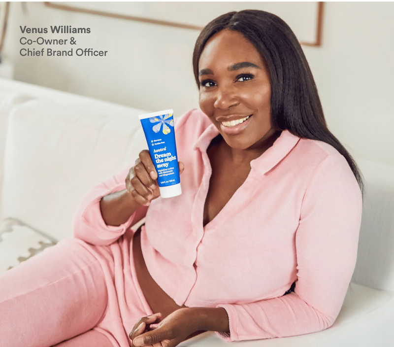 A woman in pink pajamas sitting on a bed, smiling, holding a tube of Melatonin Lotion with Magnesium for better sleep.