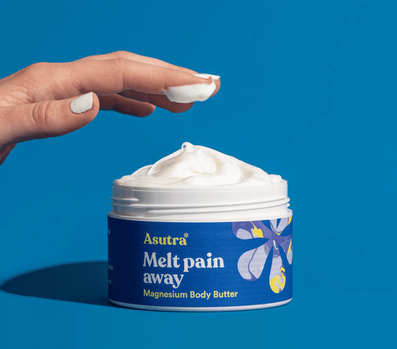 Container of Asutra Magnesium Body Butter with Capsaicin, showing a hand scooping the creamy, white moisturizer against a blue background.