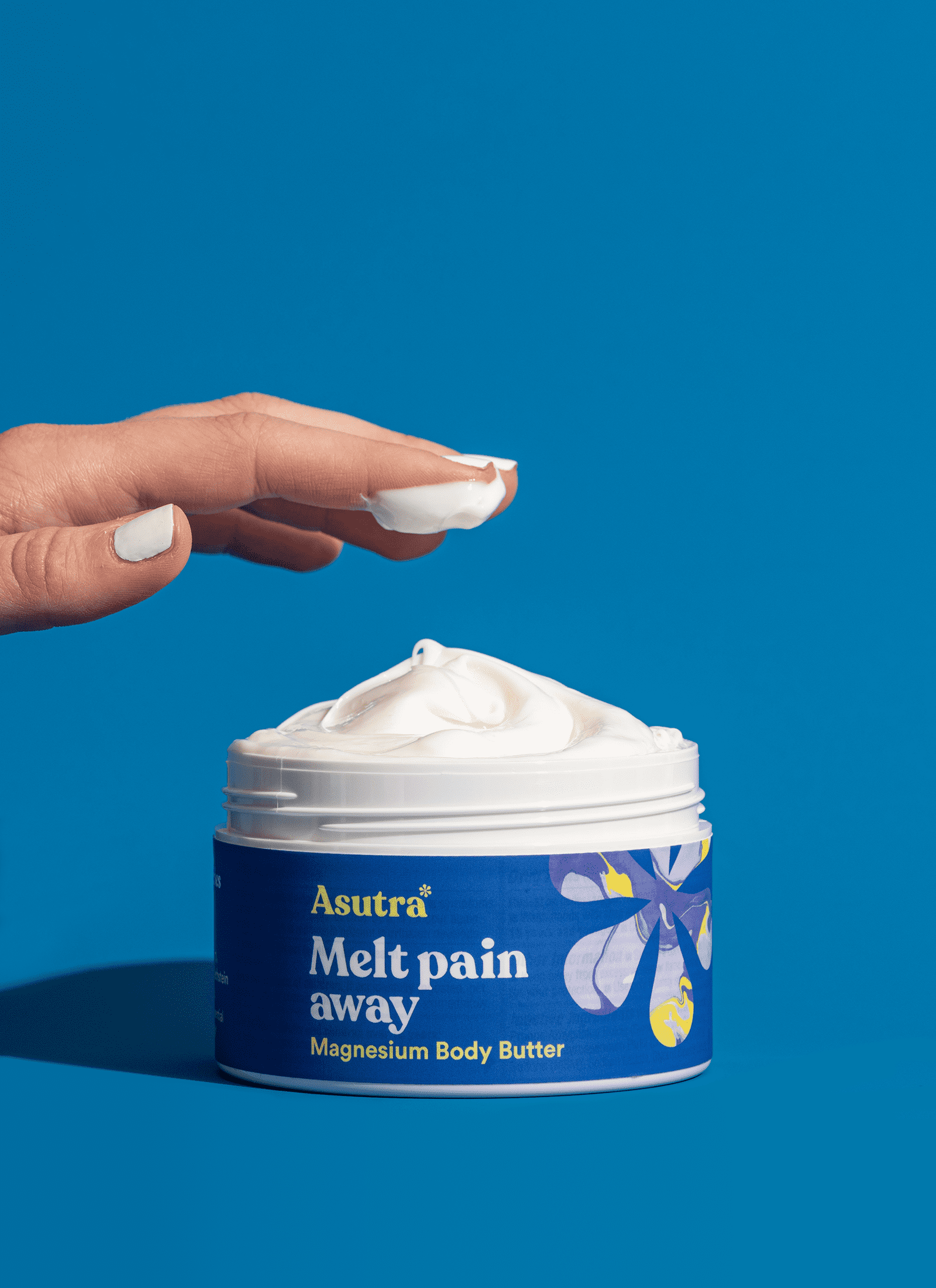 Hand scoops a small amount of magnesium body butter from an open jar against a blue background.