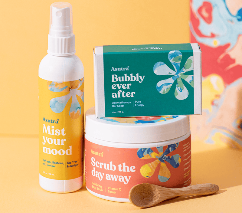 A collection of colorful skincare products including a bar soap, body scrub, mist spray, and a wooden spoon, all with vibrant floral labels.
