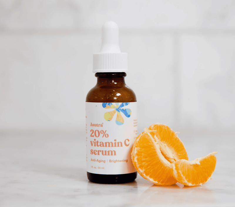 Amber glass dropper bottle of Vitamin C Anti-Aging Serum with orange slices on a white background.