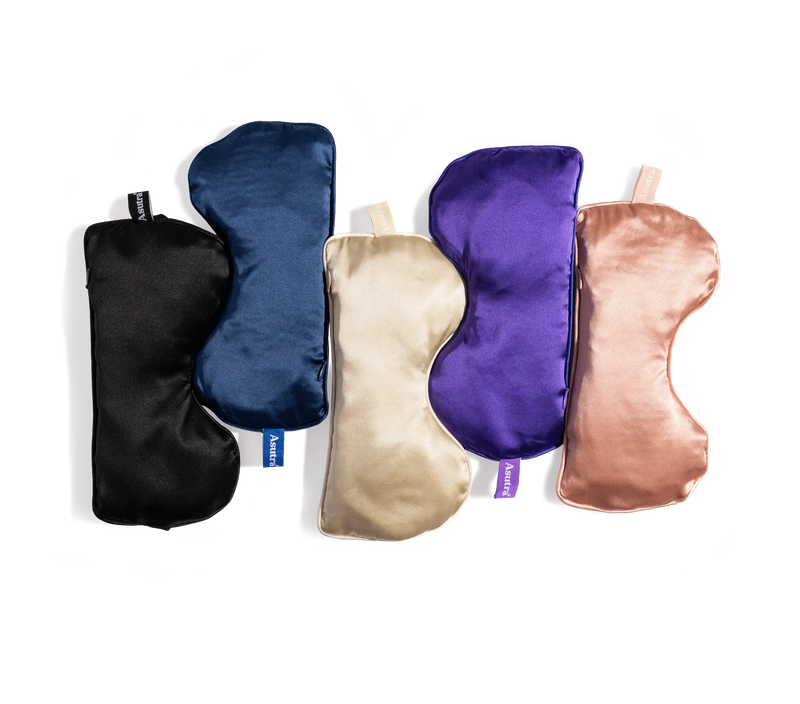 Set of five silk eye pillows in black, navy, cream, purple, and blush pink, designed for relaxation and sleep.