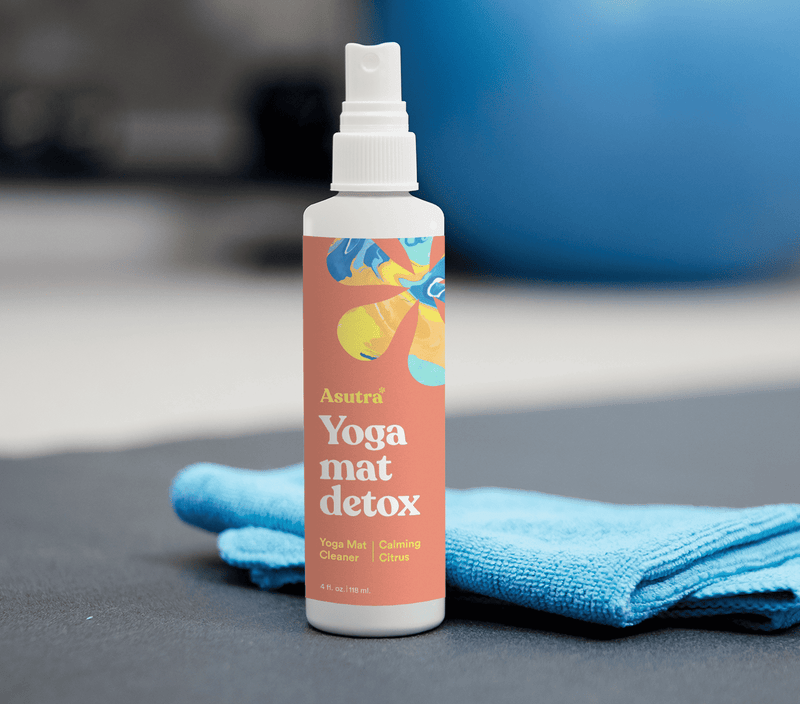 Bottle of Calming Citrus Yoga Mat Cleaner with a blue cleaning cloth on a gray surface.