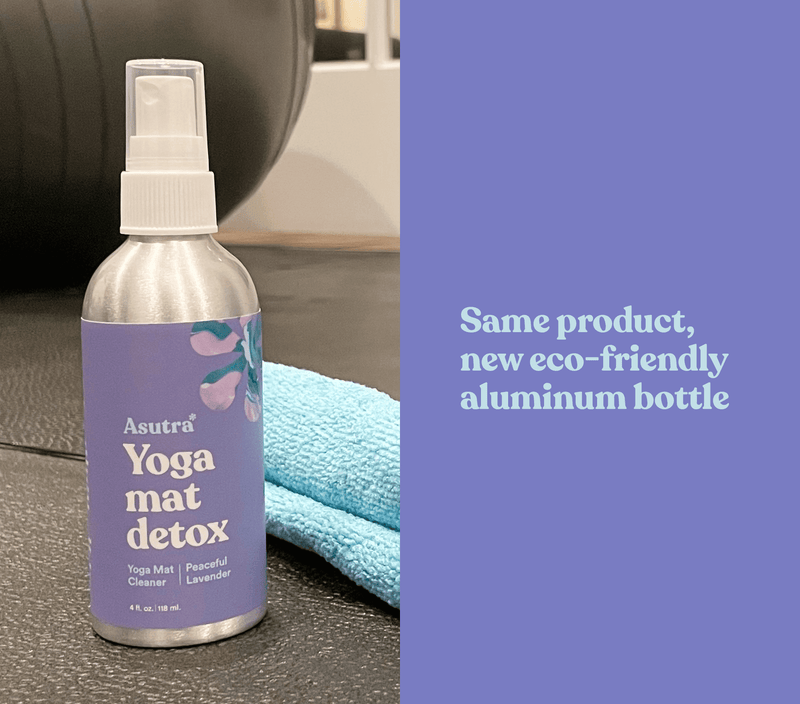 Aluminum lavender yoga mat cleaner spray bottle with a purple label, placed on a yoga mat with a blue towel nearby.