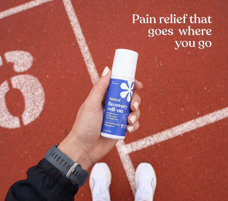 Hand holding Asutra Recovery Roll-On on a running track, highlighting portable pain relief for active lifestyles.