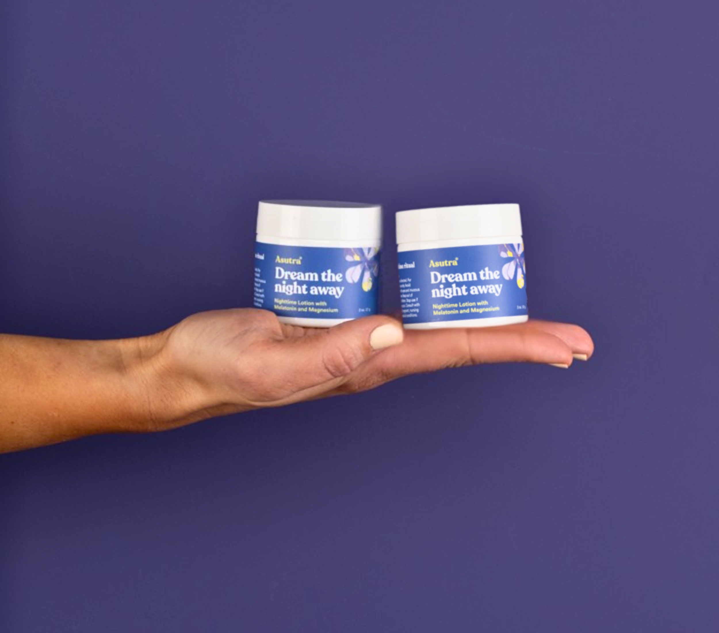 Hand holding two jars of Asutra's Dream the Night Away Lotion against a purple background, showcasing the product's calming benefits.