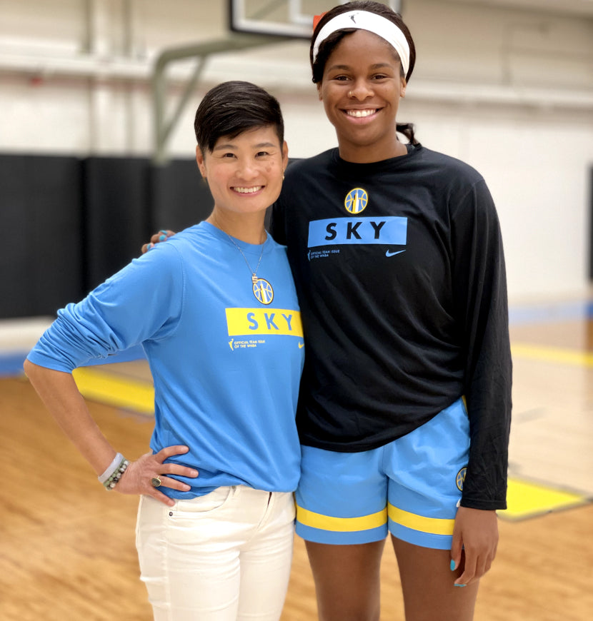 Two women, both in Chicago Sky  Women's Basketball gear, smile and pose together on a basketball court.