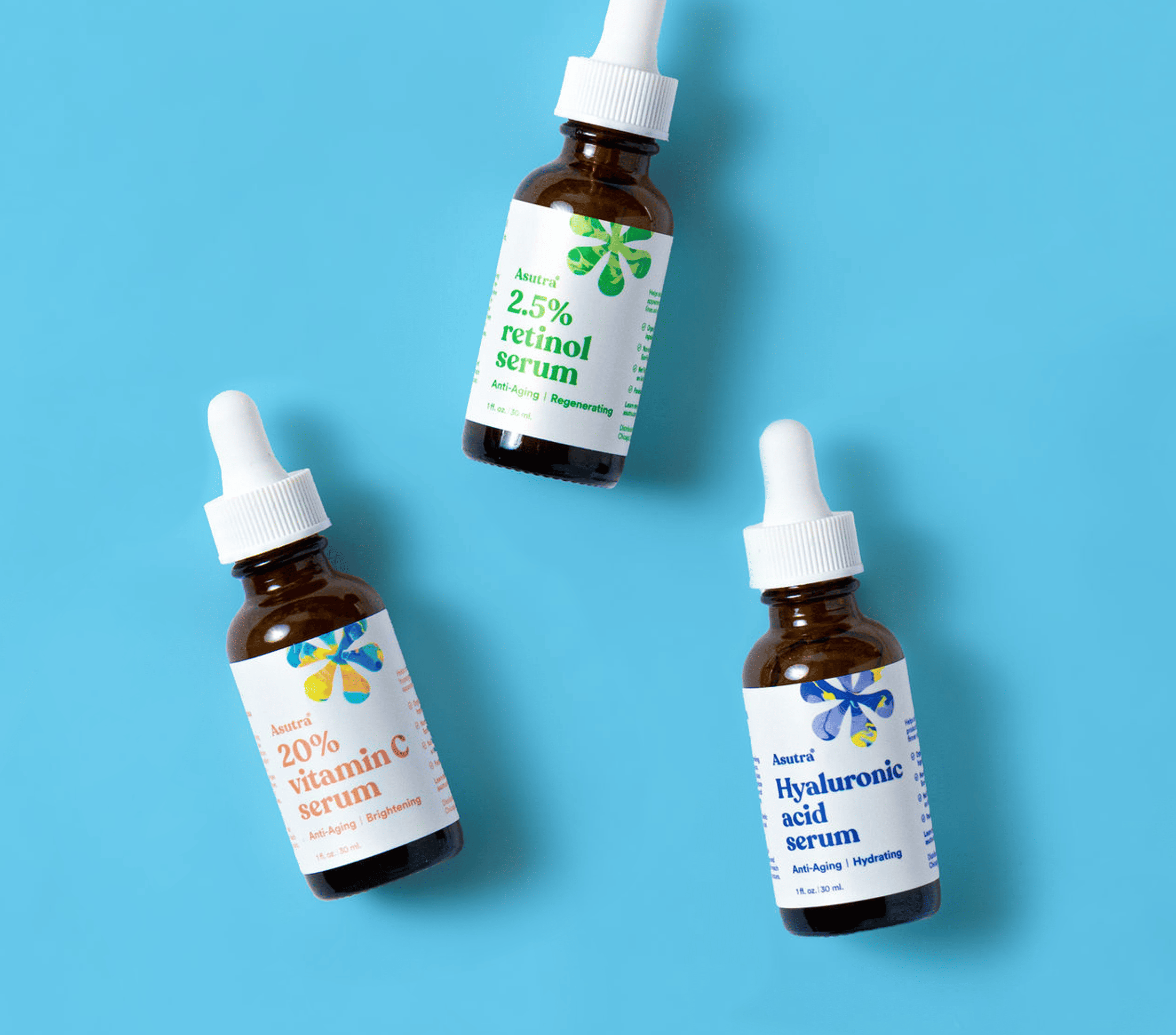 Asutra serums on blue backdrop: 2.5% retinol serum, 20% vitamin C serum, and hyaluronic acid serum, for anti-aging and hydration.