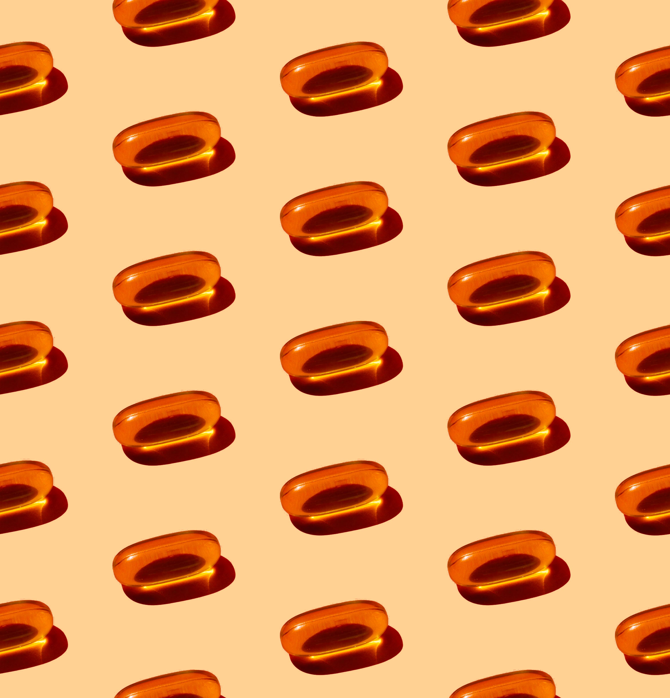 Rows of orange vitamin E capsules arranged on a light peach background.