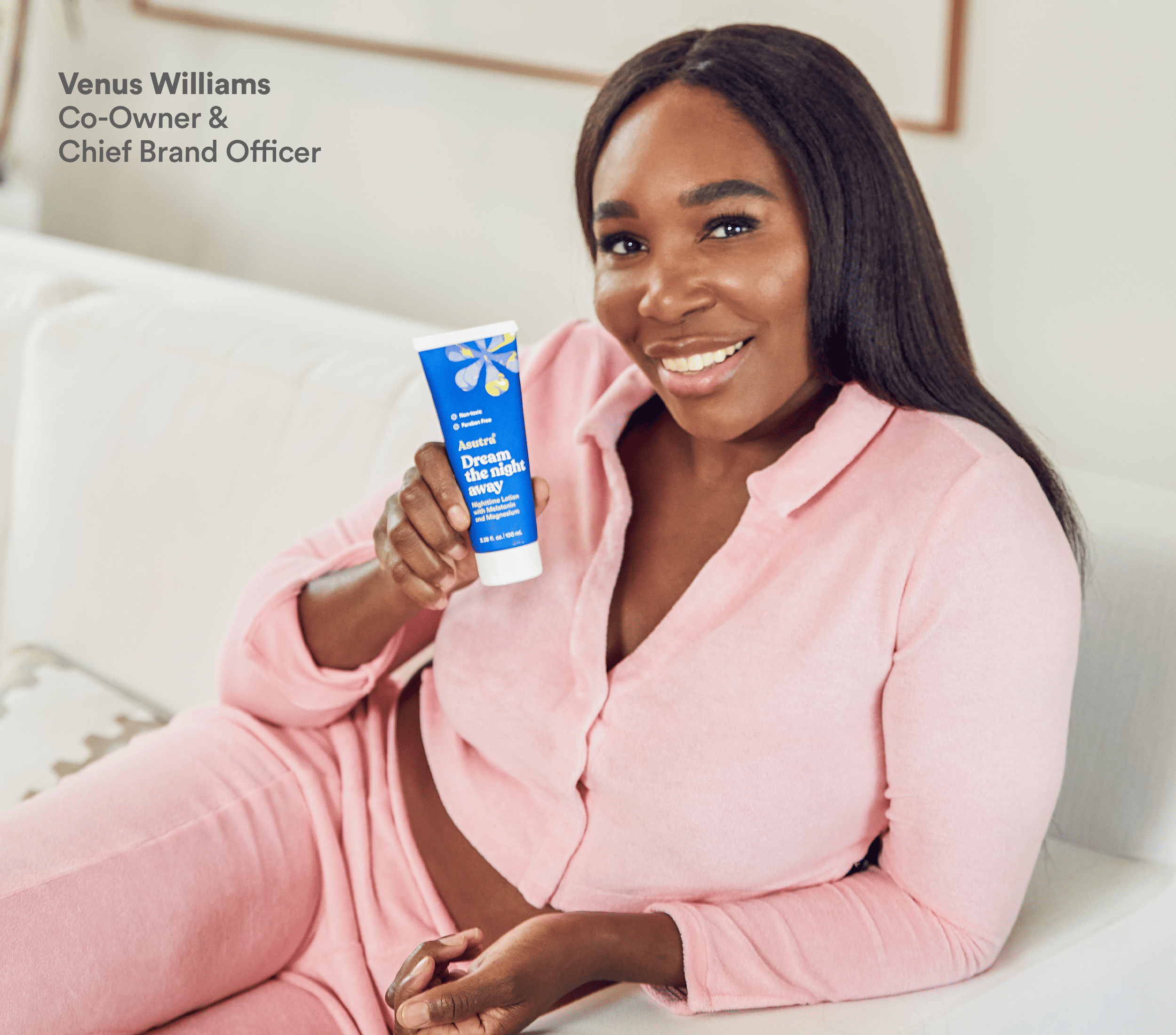 Venus Williams smiles while holding a tube of Asutra Dream the Night Away nighttime lotion, sitting on a couch.