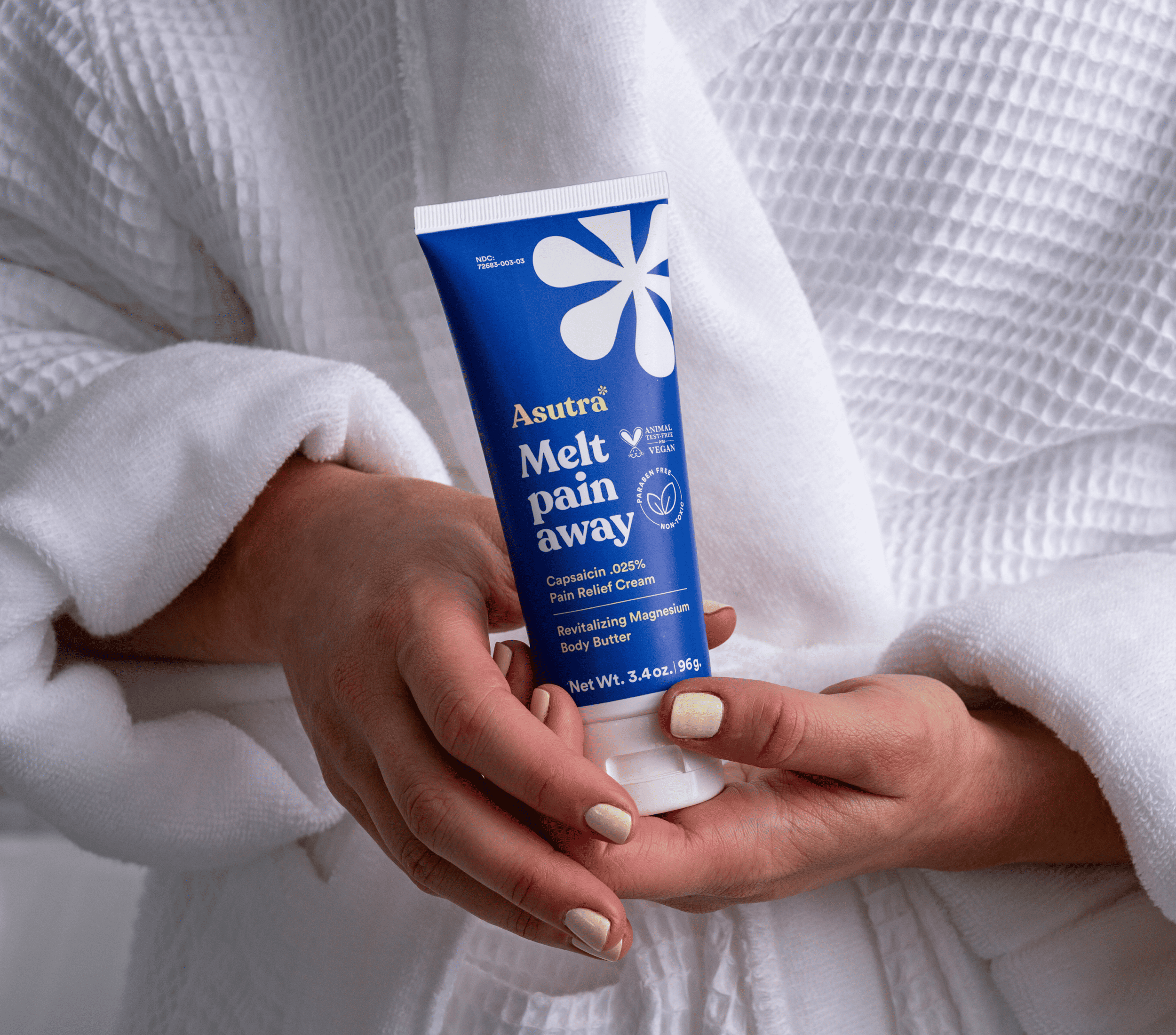 Asutra Melt Pain Away Body Butter in a tube, held by a person in a white robe, promoting pain relief and relaxation.