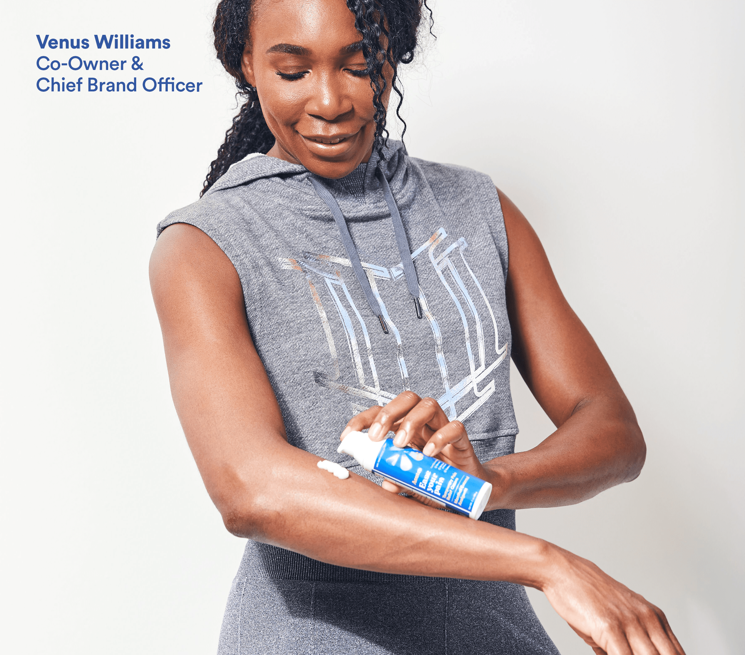 Venus Williams applies Ease Your Pain cream to her arm while wearing workout attire.